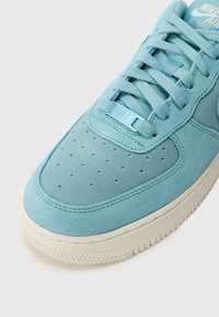 Világoskék Nike Air Force 1 sneaker, velúr felsőrésszel, perforált lábujjrésszel, lapos fűzőkkel és texturált gumitalppal.