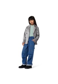 Srebrna, cekinowa marynarka z podwójnymi guzikami, zielony top oraz luźne niebieskie spodnie cargo z denimu z wieloma kieszeniami. Czarne buty dopełniają stylizację.