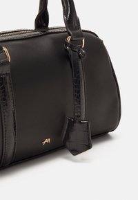 Sac à main noir avec une finition lisse et des accents en motif crocodile. Les détails en métal doré et les poignées robustes rehaussent son design.