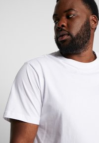 T-shirt en coton blanc à coupe regular, col rond et manches courtes. Affiche une texture lisse sans motifs ni accents visibles.