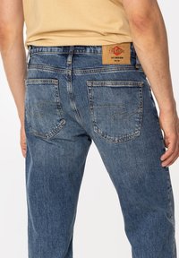 Niebieskie dżinsy z denimu o klasycznym prostym kroju, tylnymi kieszeniami z delikatnym przeszyciem oraz skórzaną naszywką marki w kolorze koniakowym na pasie.