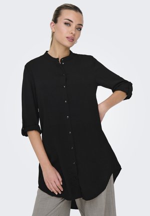 Camicia nera con colletto alto, maniche arrotolate e orlo posteriore allungato. Texture morbida, design minimale e senza pattern visibili.