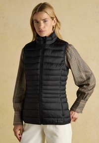 Fekete puff-berakott mellény magas gallérral, vízszintes steppelt mintával, elülső zipzárral és oldalzsebekkel; kockás inggel párosítva.