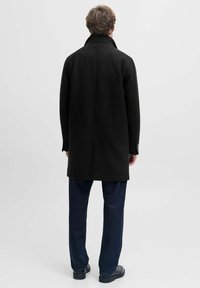 Must must ülerkood, kõrge krae, sirge lõike ja pikkade varrukatega; kantud tumedatest sinistest pükstest ja mustadest kingadest. Lihtne, minimalistlik disain.