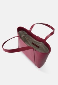 Sac fourre-tout en cuir rouge au toucher lisse, avec deux longues poignées et un intérieur spacieux doublé de tissu beige. Comprend une poche zippée.