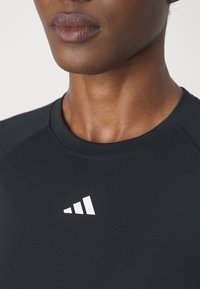Crni sportski top s okruglim izrezom, s bijelim logotipom s tri pruge na prsima. Glatka tekstura s besprijekornim dizajnerskim detaljima.