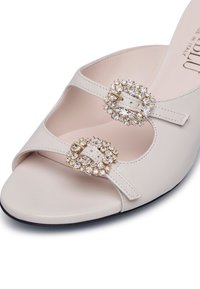 Sandal in pelle bianca con cinturini incrociati, dotato di due fibbie decorate con gemme. Design open toe e suola testurizzata. Made in Italy.