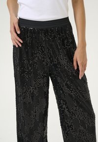 Pantaloni neri a gamba larga con decorazioni in paillettes texturizzate; fascia elastica in vita per il massimo comfort; finitura scintillante e riflessi di luce variabili.
