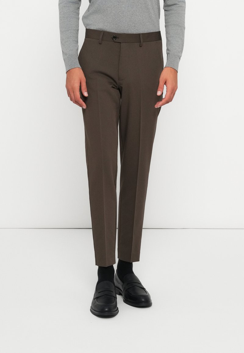 Bruna skräddarsydda byxor i slätt tyg, med slim fit, flat framsida och en enkel knappstängning. Stylerade med svarta loafers.
