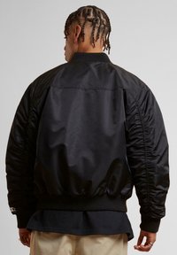 Jachetă bomber neagră cu un finisaj neted și lucios. Prezintă manșete și tiv ribbate, mâneci pufose și un design curat, minimalist.
