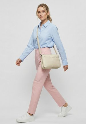 Vrouw die loopt, gekleed in een blauw geruit overhemd, roze broek, witte sneakers en een beige schoudertas draagt.