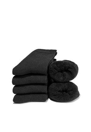 Vier Paar schwarze Socken flach gefaltet links gestapelt, zwei Paar schwarze Socken rechts aufgerollt vor weißem Hintergrund.