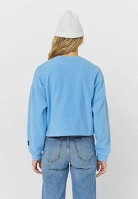 Felpa blu a maniche lunghe e taglio corto, con scollatura rotonda e finitura testurizzata. Indossata con jeans chiari a vita alta.