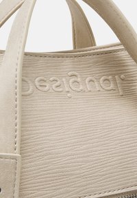 Beige strukturiertes Lederhandtasche mit kurzen Griffen, ausgestattet mit geprägt Logo, glatten Nähten und dezentem Maserungsmuster.