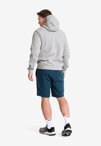 Grå sweatshirt med huva, långa ärmar och ribbade muddar, parat med mörkblågröna shorts. Stylar med träningsskor och vita strumpor.