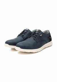Zapatos sintéticos azul marino con un acabado suave, suelas de goma blanca y cordones negros. Presentan un forro a rayas y un pequeño logotipo en la lengüeta.