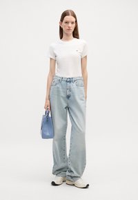 Camiseta blanca de manga corta, jeans de tiro alto y pierna ancha en azul claro, bolso azul y zapatillas deportivas con detalles en negro.