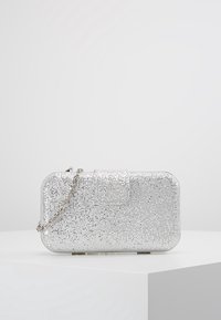 Pochette en sequins argentés avec une forme rectangulaire, fermeture à rabat magnétique et une bandoulière en chaîne argentée. La surface texturée réfléchit la lumière.