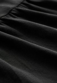 Czarna tkanina o miękkiej fakturze i subtelnym połysku, z fałdami marszczonymi, tworzącymi delikatny opadający kształt i gładką powierzchnię.