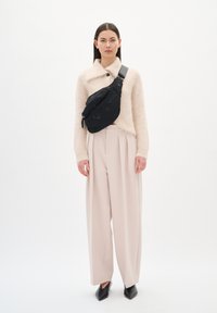 Fekete díszített válltáska egy világos bézs bolyhos kardigánon, magas derekú, széles lábú krémszínű nadrággal és hegyes fekete cipővel párosítva.