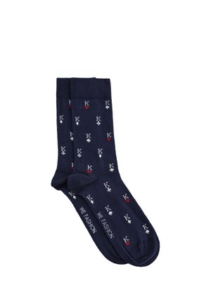 Chaussettes bleu marine avec un motif répété de symboles de cartes à jouer et d'initiales en blanc et rouge. Tissu doux avec un bord-côte côtelé.