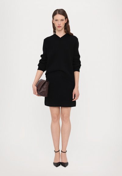 Maglione nero a collo a V e gonna nera aderente, abbinati a una clutch in pelle marrone scuro e scarpe nere con punta. Texture liscia e design semplice.