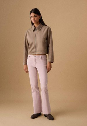 Smeđa skraćena jakna sa zatvaračem i ovratnikom ukrašenim zakovicama, uparena s svijetlo ružičastim zvonastim trapericama i sivim čizmama. Glatka tekstura, moderan dizajn.