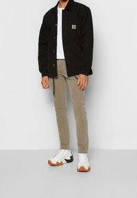 Svart kordjacka med framfickor, vit t-shirt, beige slim-fit byxor och vita sneakers med svarta och orange sulor.