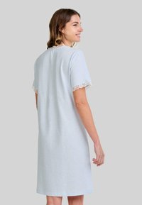 Mujer vistiendo un vestido de longitud hasta la rodilla en azul claro, con mangas cortas acentuadas con encaje y un cuello de encaje, de perfil contra un fondo liso.