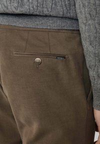 Brązowe bawełniane spodnie z tylną kieszenią z guzikem i małą metką z napisem "HACKETT". Na górze znajduje się fakturowany szary sweter.