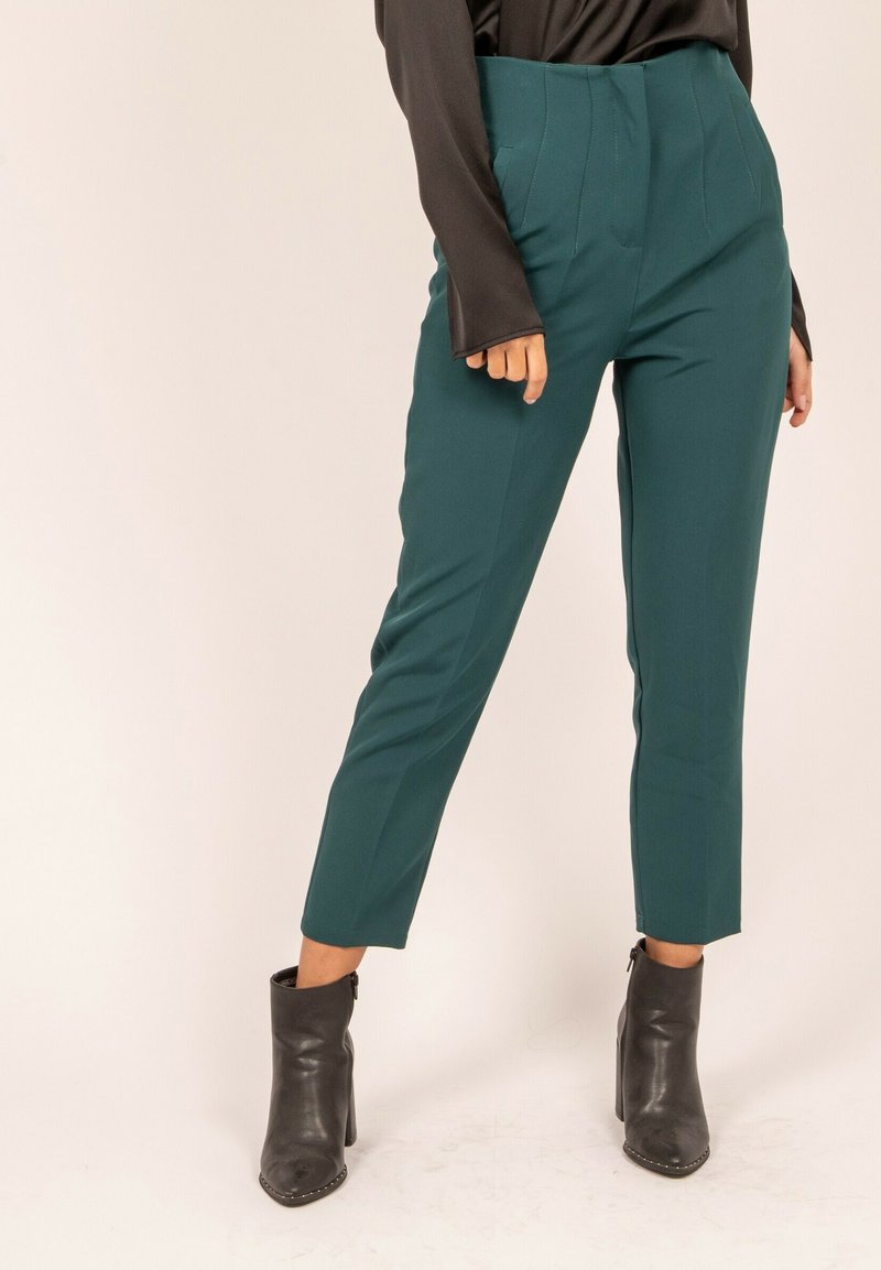 Pantalons taille haute teal au design épuré, avec des coutures verticales, des jambes fuselées et un tissu texturé, associés à des bottines noires.