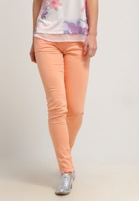 Persikofärgade skinny jeans i kombination med en blommig topp, som har en mjuk textur och smal passform. Outfiten kompletteras av glänsande silverfärgade skor.