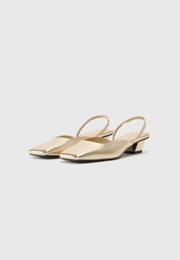 Scarpe slingback metalliche oro con punta quadrata, tacco basso a blocco e superficie liscia. Presentano una cinghia alla caviglia per supporto e stabilità.