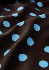 Tissu marron avec des pois bleu clair de forme irrégulière, montrant des plis doux et des détails de texture.