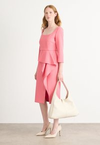 Robe rose avec des manches trois-quarts, détail peplum et fente avant. Associée à un sac hobo crème et des chaussures à talons nus.