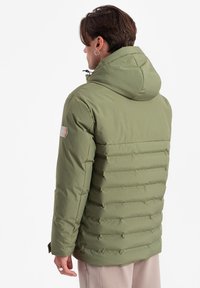 Olivově zelená péřová bunda s kapucí, s prošívanou texturou a detaily na ramenou. Zapínání na zip a dlouhé rukávy.