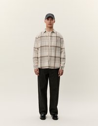 Beige karierte Flanellhemd mit Knopfverschluss, dunkle Jeans und schwarze Schuhe. Ergänzt durch eine dunkle Baseballmütze. Minimalistisches Design.
