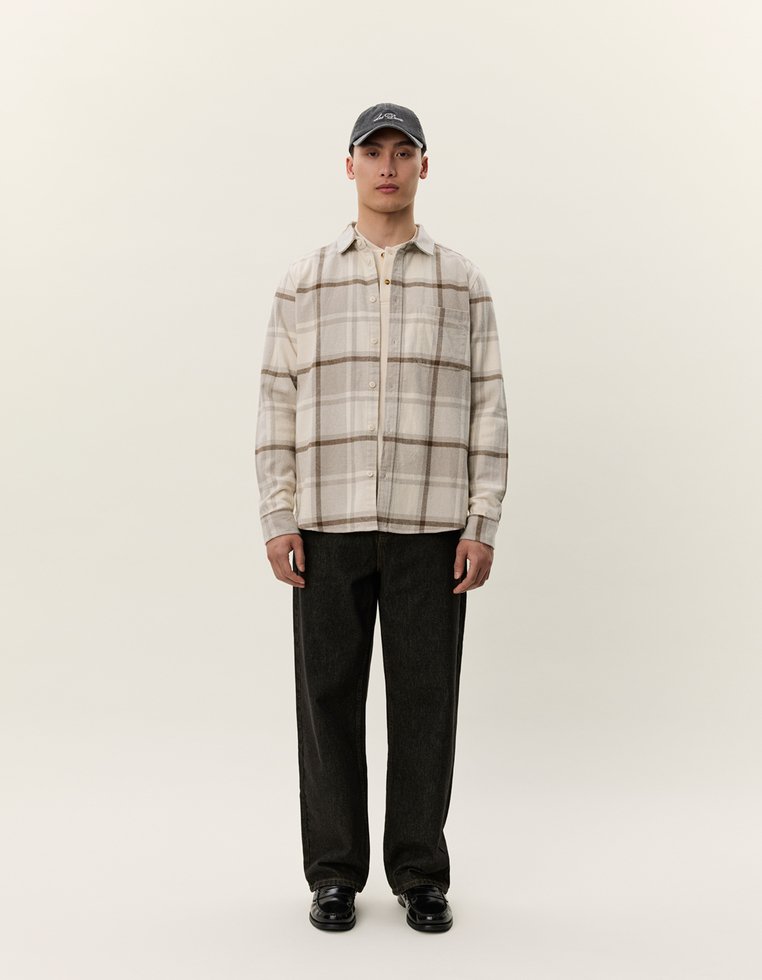 Beige karierte Flanellhemd mit Knopfverschluss, dunkle Jeans und schwarze Schuhe. Ergänzt durch eine dunkle Baseballmütze. Minimalistisches Design.
