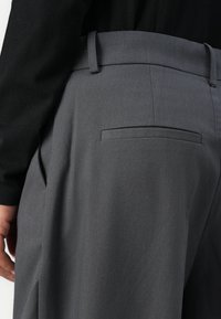 Gray trousers featuring a sleek design with a smooth texture, flat back pockets, and a tailored waistband.