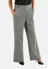 Pantaloni grigi a gamba larga realizzati in tessuto morbido, con tasche frontali e chiusura con bottone, abbinati a scarpe con tacco alto nere.