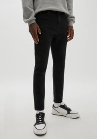 Vaqueros de mezclilla negra con corte ajustado, que cuentan con cinco bolsillos, una textura sutil, y combinados con zapatillas bajas en blanco y negro.