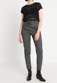 Svart spetskortärmad topp med geometriska utskärningar, parat med grå hounds-tooth tapered byxor och svarta ankelskor med en glansig yta.