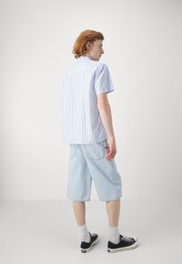 Short-sleeve, light blue and white striped button-up shirt made of cotton, paired with light denim shorts and black sneakers.