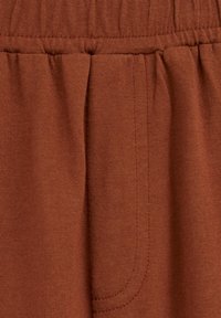Brun bomullstyg med en rynkad midja och subtil sömnad. Inkluderar en sidofickdetalj med mjuk textur.