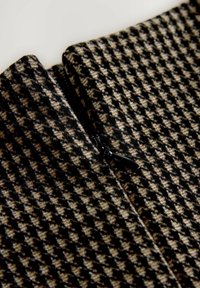 Nærbillede af brun og sort hundetandsmønster stof med en delvist synlig sort lynlås.