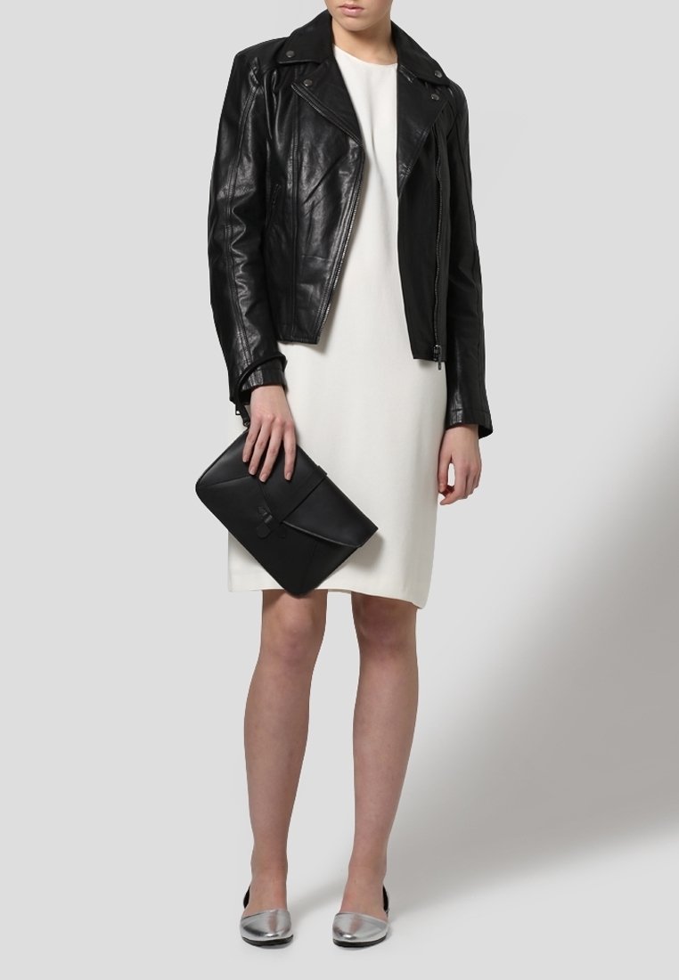 Veste de motard en cuir noir portée sur une robe blanche, associée à une pochette noire et des chaussures plates argentées. Textures lisses et contraste des couleurs.
