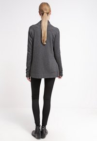 Cárdigan largo de manga larga en gris oscuro con cuello, textura suave y aberturas laterales, combinado con leggins negros y botines.