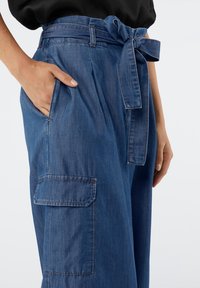 Pantalones de mezclilla con una cintura alta con cinturón, que cuentan con un bolsillo lateral y un corte holgado. La tela es de un azul medio con ligera textura.