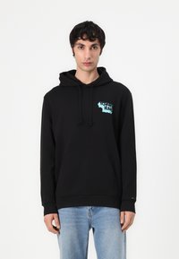 Zwarte hoodie van zachte stof, met een voorkant kangaroo zak en een blauw grafisch logo op de borst. Lange mouwen met geribde manchetten.