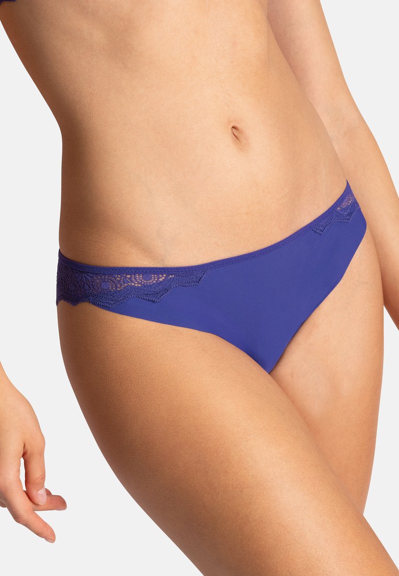 Sous-vêtements violets en tissu lisse, avec une finition en dentelle le long de la taille, mettant en valeur un design à bords festonnés.